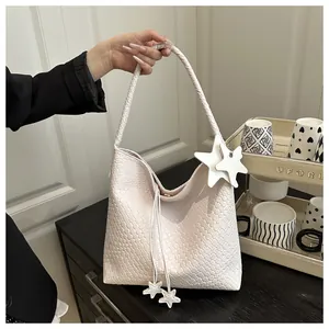 Détail du sac hobo tressé blanc avec deux breloques étoiles et une finition texturée