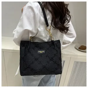Detail of black textured jacquard tote bag with golden chain and branding tag