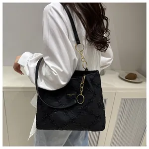 Detail of black textured tote bag featuring leather logo tag and gold chain strap link