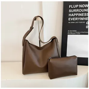 Detail view of large dark brown leather tote bag with matching zippered pouch on white stand