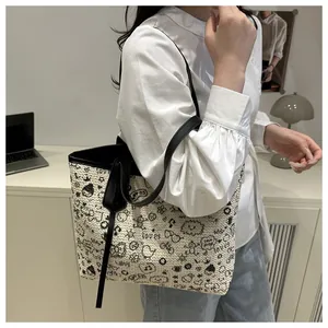 Detail of woven tote bag featuring playful black graffiti patterns and slim shoulder straps