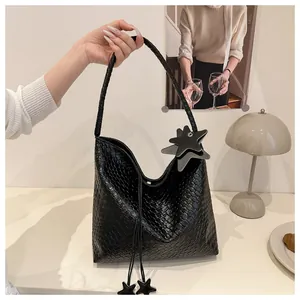 Détail du sac hobo en cuir tressé noir avec pendentif étoile, pompons et bandoulière tressée