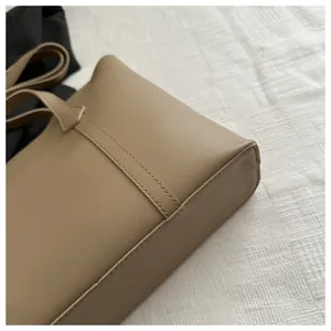 Macro shot of double-stitched leather handle and bottom corner on khaki tote bag