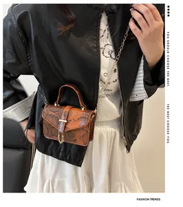 Detail of brown snake skin texture and gold V-shaped buckle on small crossbody bag