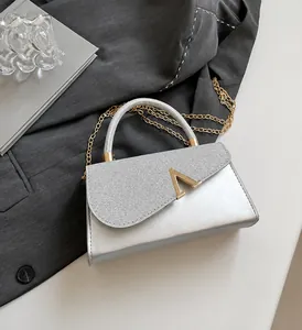 Detail view of silver mini handbag with sparkly flap, V-metal clasp and gold chain strap