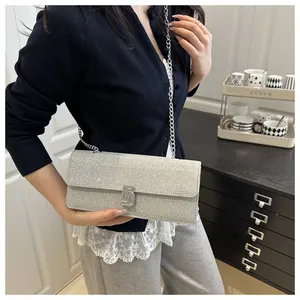 Close-up of a silver sequin baguette bag with a metallic chain strap on a model