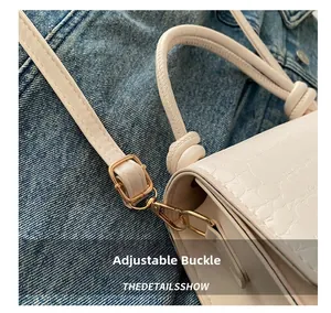 Détail d'un sac à main blanc à motif crocodile avec boucle dorée et bandoulière réglable