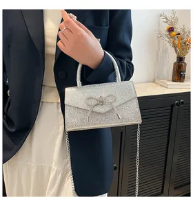 Close-up of glitter silver evening handbag featuring a sparkling crystal bow and metal chain