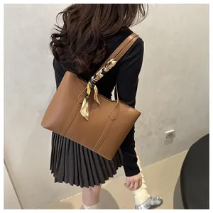 Detailed back view of a brown leather tote bag with a patterned silk scarf on strap