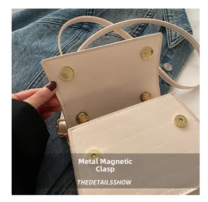 Détail du fermoir magnétique doré sur un sac à main à motif crocodile de couleur crème