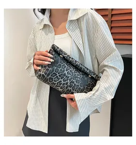 Detail of leopard print handbag with metal clasp held by a model in striped shirt