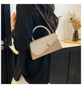 Elegant beige top handle bag with a gold V-shaped buckle and metallic chain strap