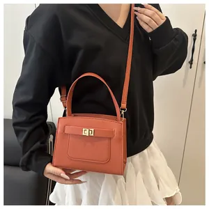 Detail einer orangefarbenen Saffiano-Ledertasche mit goldenem Drehverschluss am Model