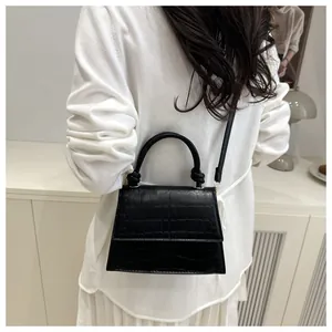 Mini sac carré noir à motif crocodile porté à l'épaule dans un décor très minimaliste