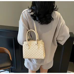 Detail view of beige retro tote with all-over M pattern and shoulder strap worn by model