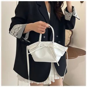 Detailed view of white pleated handbag featuring a decorative bow and curved handle