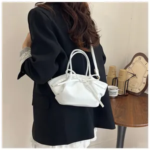 White pleated leather bag with bow detail held by model in a cozy interior scene