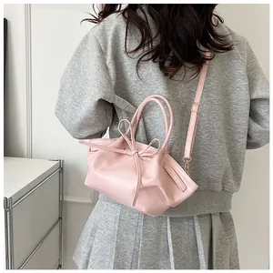 Pink bow handbag with cross-body strap shown from behind on a model for size perspective