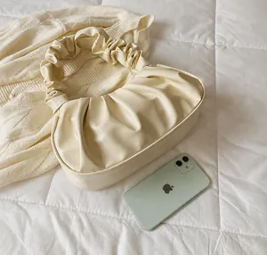 Close-up of cream pleated cloud bag next to an iPhone showing compact size and texture