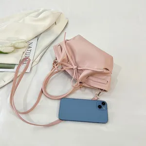 Pink bat bag with drawstring bow and shoulder strap shown with a phone for scale