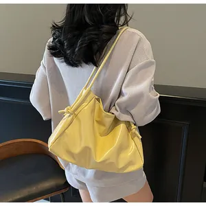 Detail of yellow glossy tote bag with unique knot shoulder strap on female model