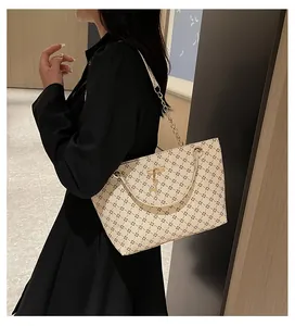Detalle del bolso tote crema con estampado de trébol y correa de cadena dorada fina