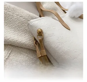 Gros plan sur le sac blanc avec gaufrage artistique, boucles dorées et sangle kaki