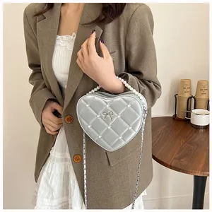 Silver quilted heart-shaped bag with pearl handle and metal chain shown on model