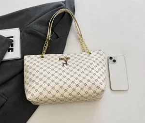 Detalle del bolso tote monograma con cadena dorada, dije de ciervo y comparación con smartphone