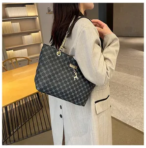 Bolso tote grande con monograma gris, cadena dorada y colgante de ciervo en una modelo