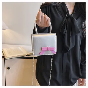 Détail du mini sac carré argenté avec nœud rose porté par un mannequin à la main