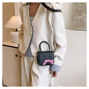 Vue détaillée du mini sac carré noir avec nœud rose et bandoulière en chaîne