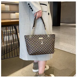 Detalle de bolso tote marrón con monograma, colgante de ciervo dorado y cadena