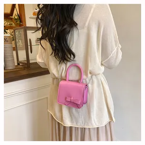 Mini sac bandoulière rose avec nœud porté par un mannequin dans un café chic