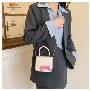 Détail du mini sac bandoulière crème avec nœud rose et chaîne argentée sur modèle
