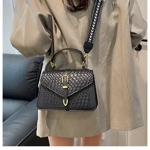Detail view of black woven texture handbag with golden clasp and geometric woven strap