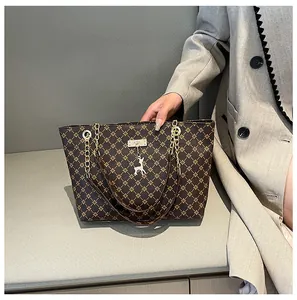 Detalle de un bolso tote marrón con estampado floral, asa de cadena y colgante de ciervo plata