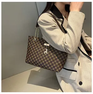 Detalle del elegante bolso tote con monograma, correa de cadena dorada y dije de ciervo