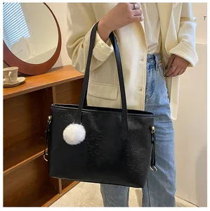 Détail du sac cabas en cuir noir avec gaufrage et un pompon en fausse fourrure blanche