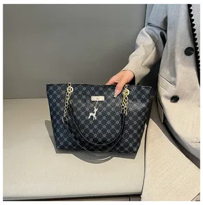 Detalle de bolso tote negro con estampado, cadena dorada y colgante de ciervo