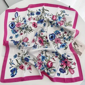 Detailed view of floral silk-feel square scarf with rose pink borders on white table