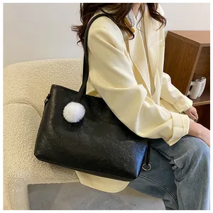 Détail d'un sac cabas noir avec motifs en relief et pompon blanc sur modèle