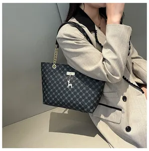 Detalle de bolsa tote gris con monograma, cadena dorada y colgante de ciervo plateado