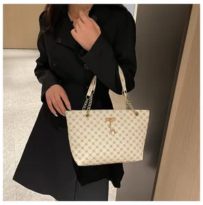 Detalle del bolso tote crema con patrón geométrico, asa de cadena y colgante de jirafa