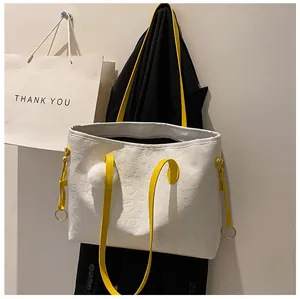 Détail du cabas blanc embossé avec poignées jaunes, pompon et anneau métallique doré