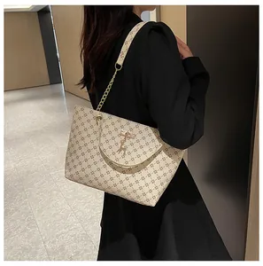 Bolso tote beige con estampado floral y cadena dorada mostrado en el hombro del modelo