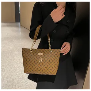 Detalle de bolso tote marrón con estampado, cadena dorada y colgante de ciervo