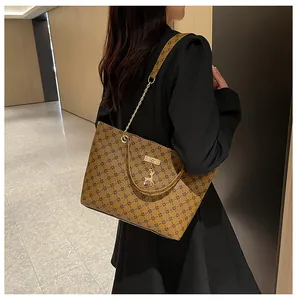 Bolso tote marrón con monograma, cadena dorada y colgante de ciervo en el hombro de la modelo