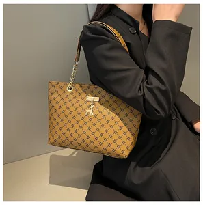 Bolso tote marrón con monograma, colgante de ciervo dorado y correa de cadena en modelo
