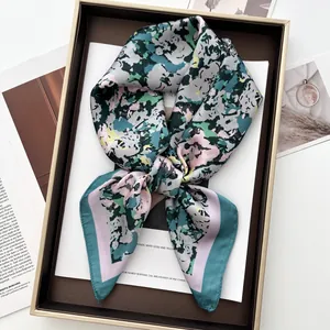 Detailed close-up of floral printed silk-like scarf with green stitched edges in a gift box